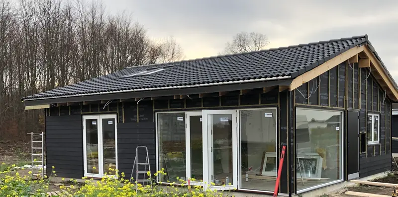 Hus med sort tegltag og hvide vinduer, sort bræddebeklædning under opsætning over vindspærren på gavlen