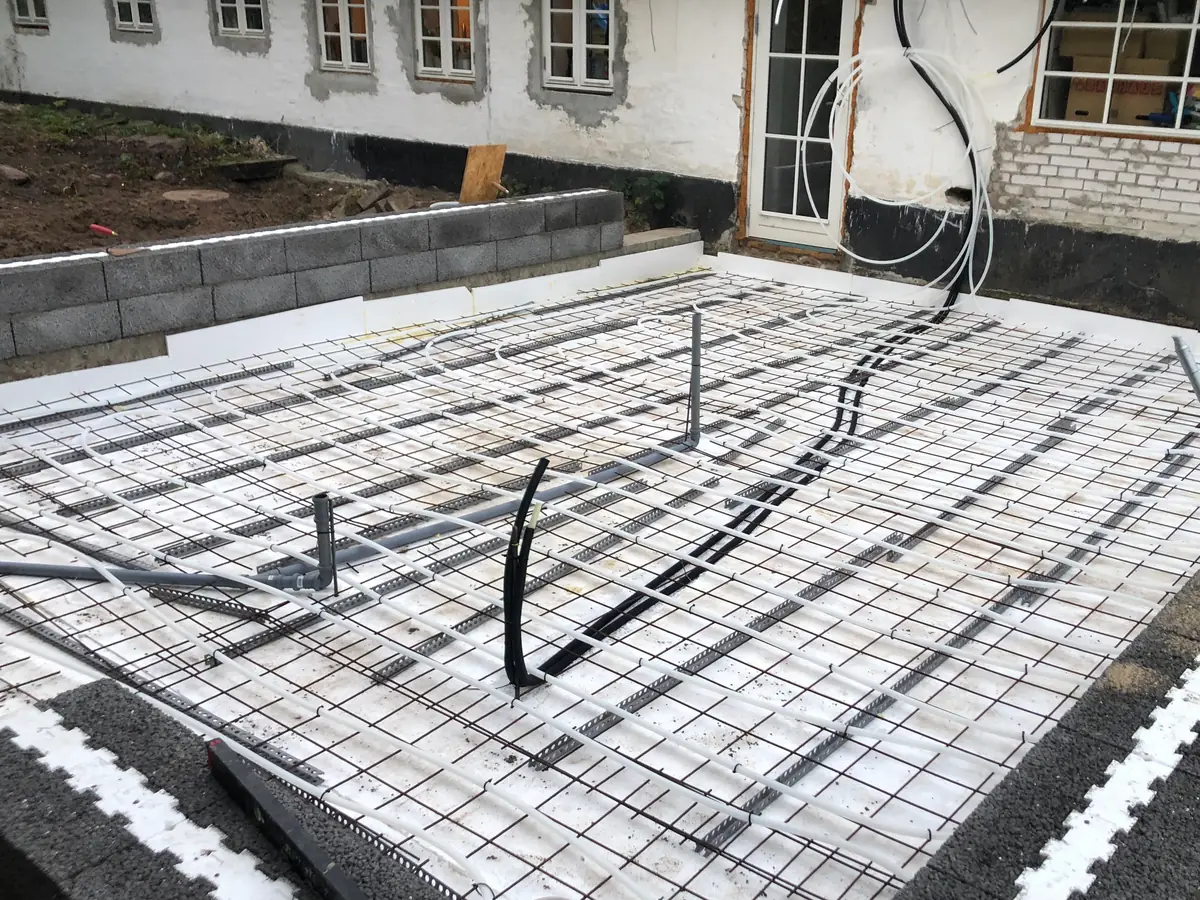 Terrændæk klar til støbning med hvid isolering, armeringsnet, rør i dækket og letklinkerblokke foran hvidkalket længe