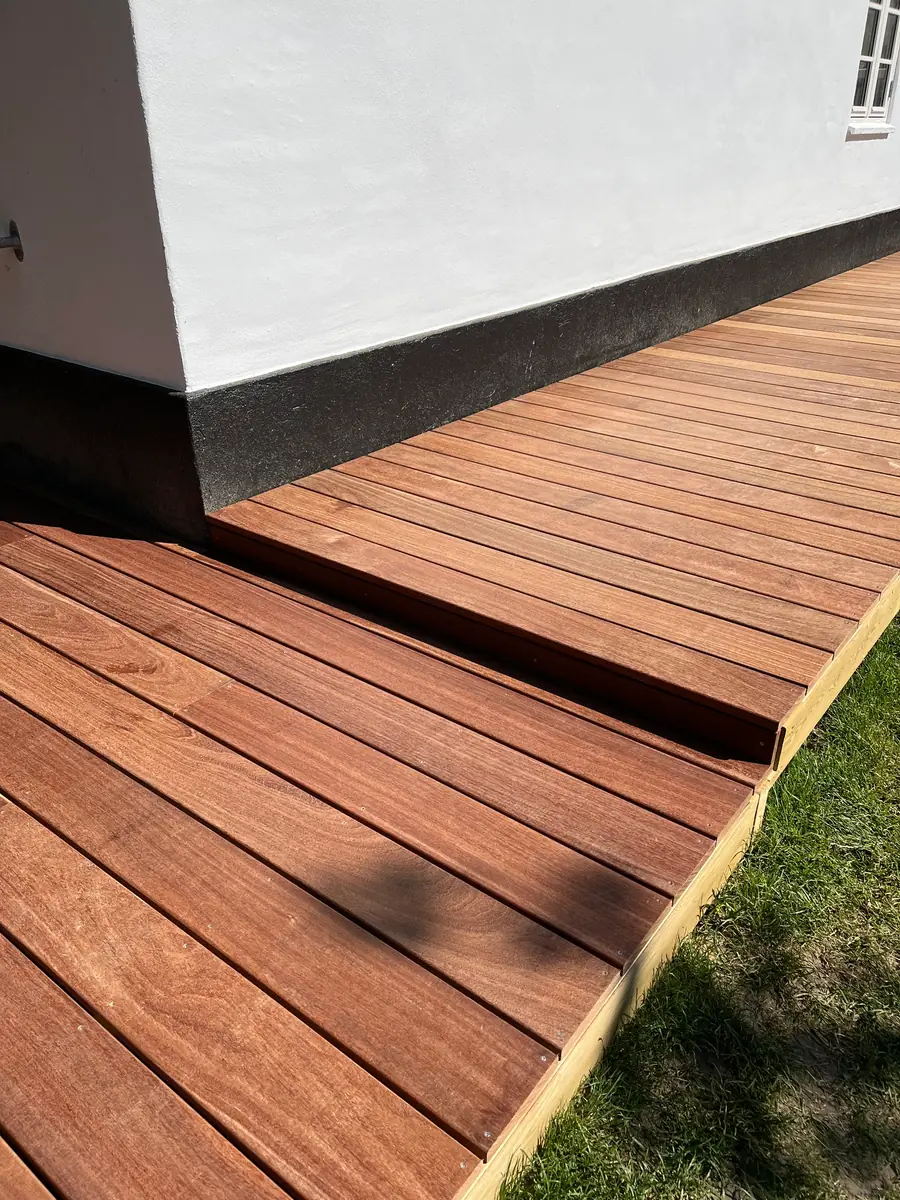 Terrassebrædder møder den sorte sokkel ved hushjørnet, trin ned til nederste dæk og trykimprægneret kantbræt